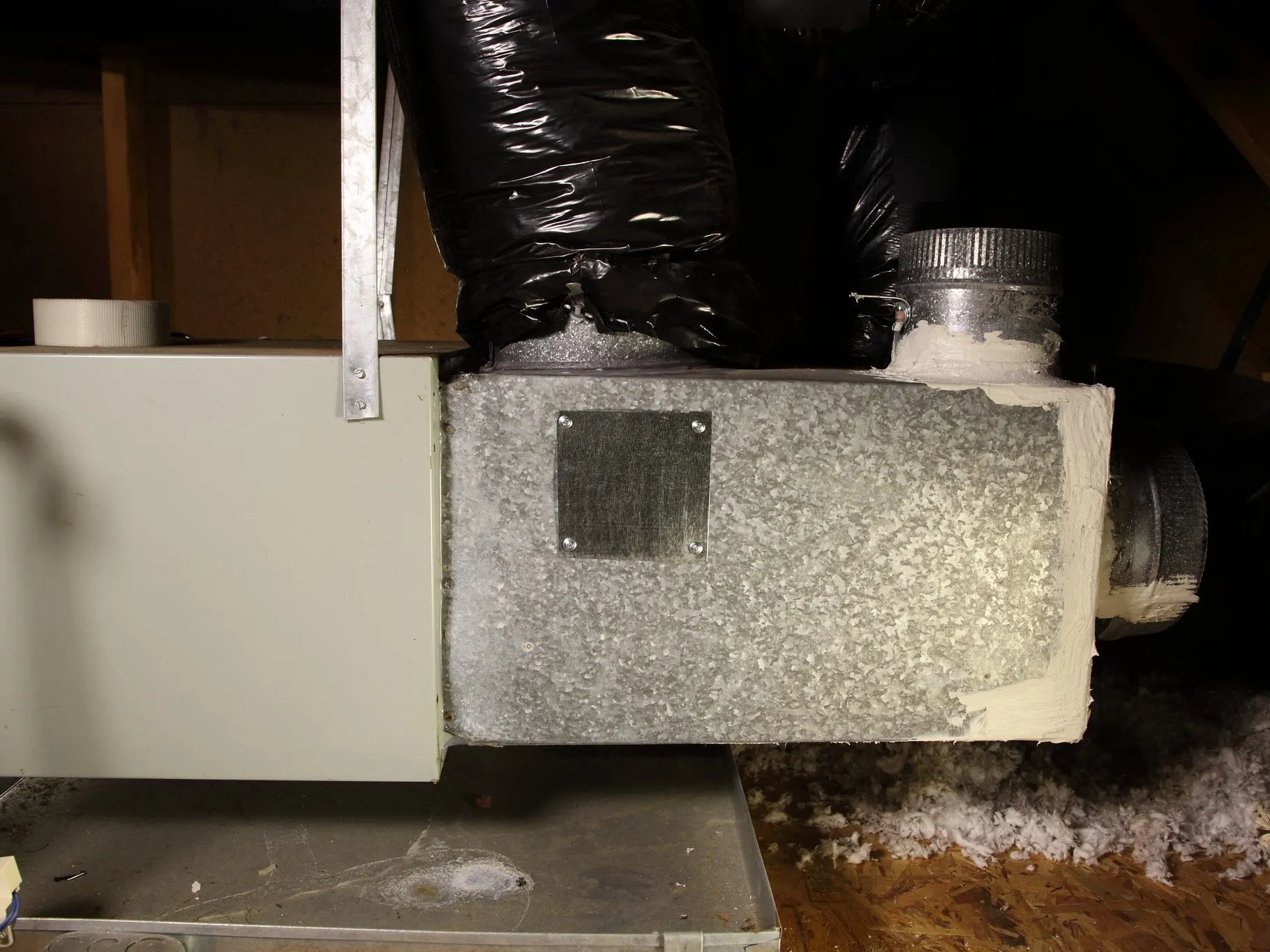 An air handler in an attic, set in a metal drain pan, with a sheet metal plenum and insulated flexible ductwork.