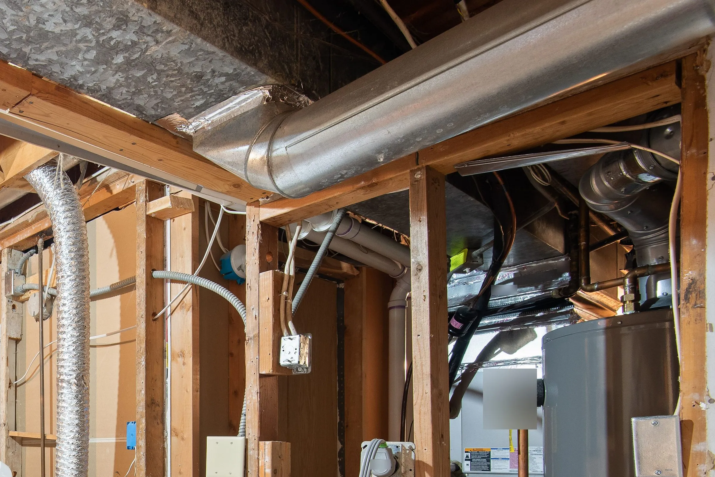 Sheet-metal ductwork, white plastic vent pipes and a gas line above a furnace and water heater in an unfinished basement
