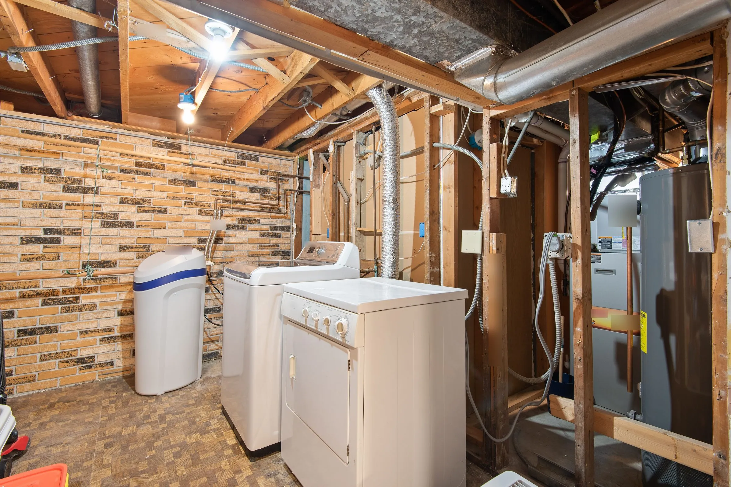An unfinished basement utility area with a washer, dryer and water softener, and a gas furnace and water heater behind the framing