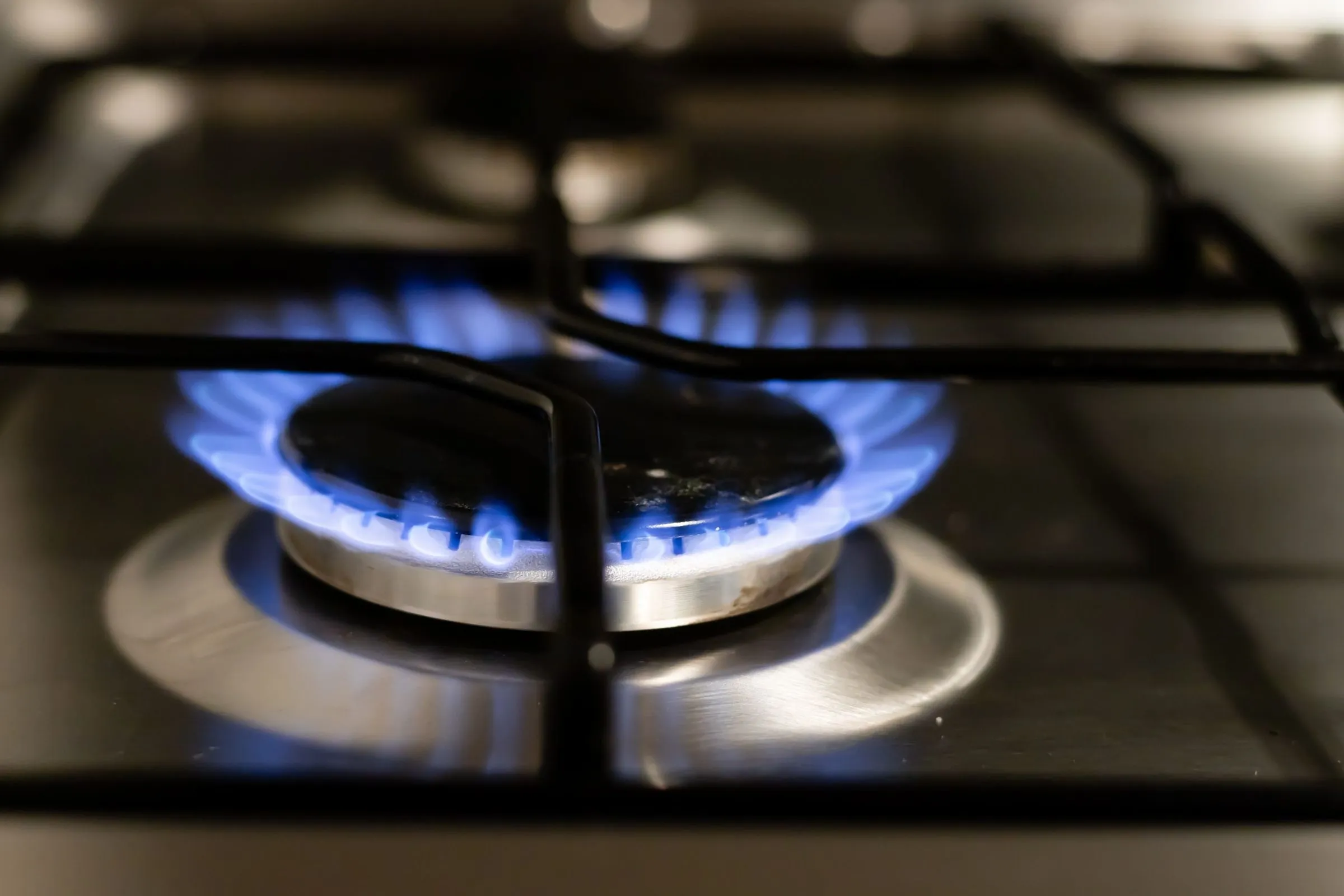A gas stove burner under a black iron grate, burning with an even ring of steady blue flames