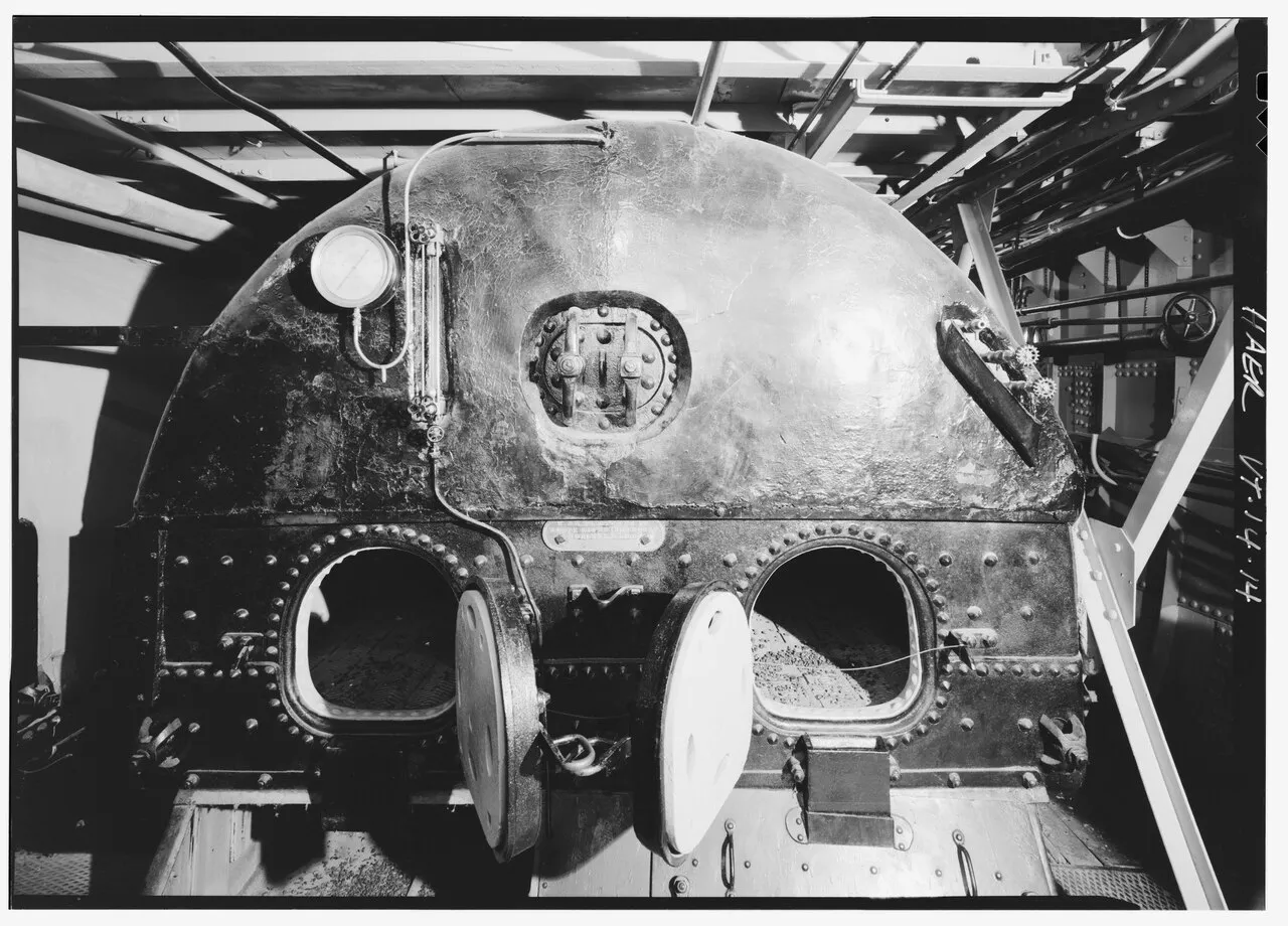 A historic industrial steam boiler with a round pressure gauge and a vertical glass water level tube on its front, shown here to illustrate what a sight glass looks like