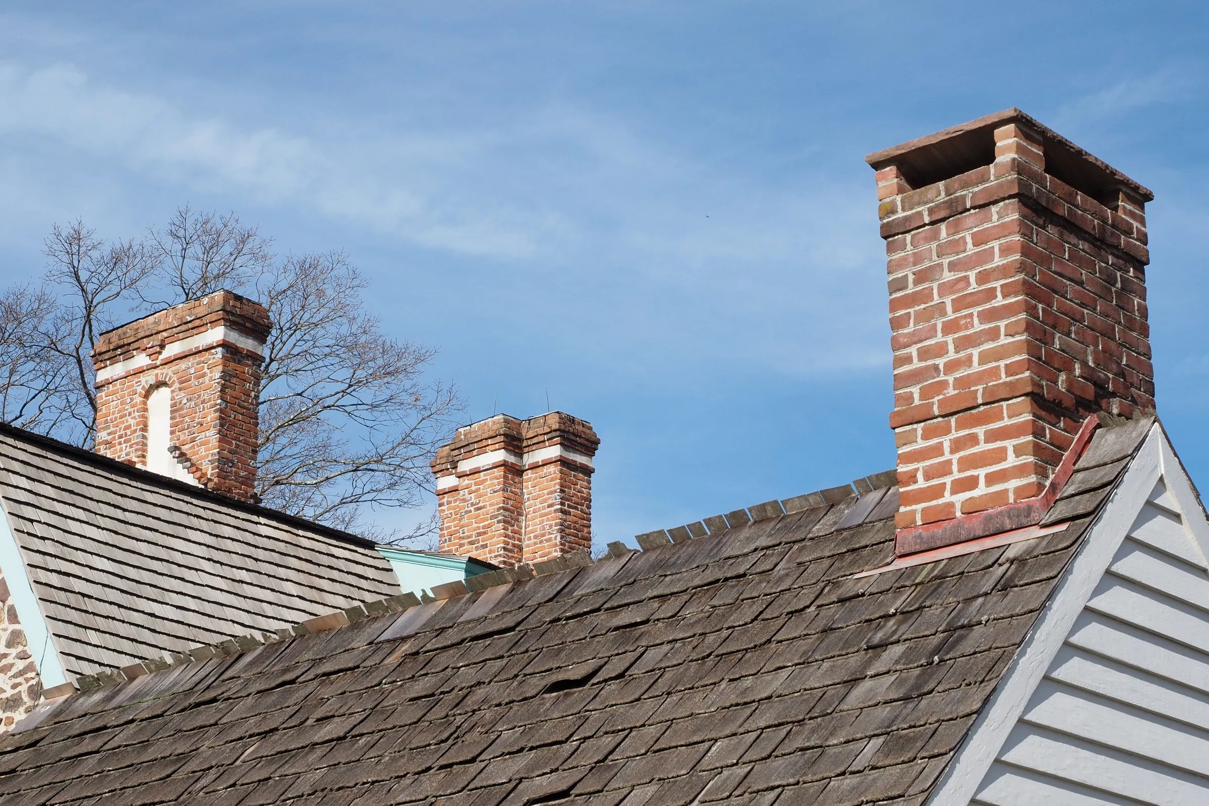 Old brick chimneys rising above the wood shingle roof of an older house against a blue sky