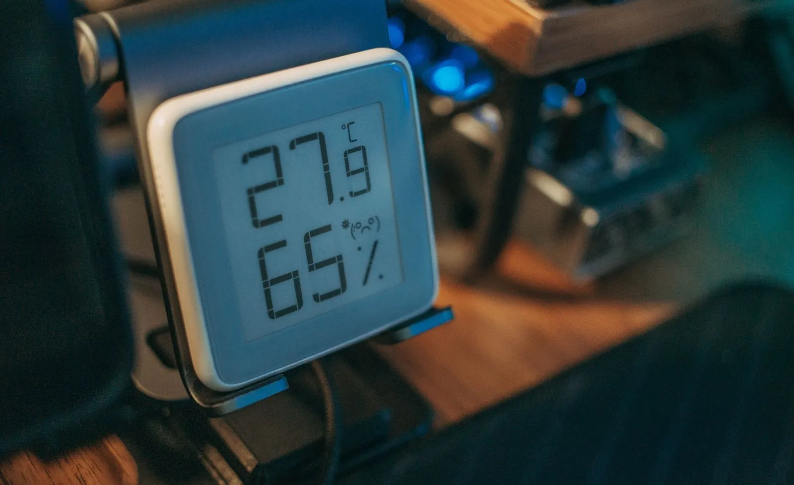 A digital hygrometer display on a desk showing the room temperature and relative humidity as numbers
