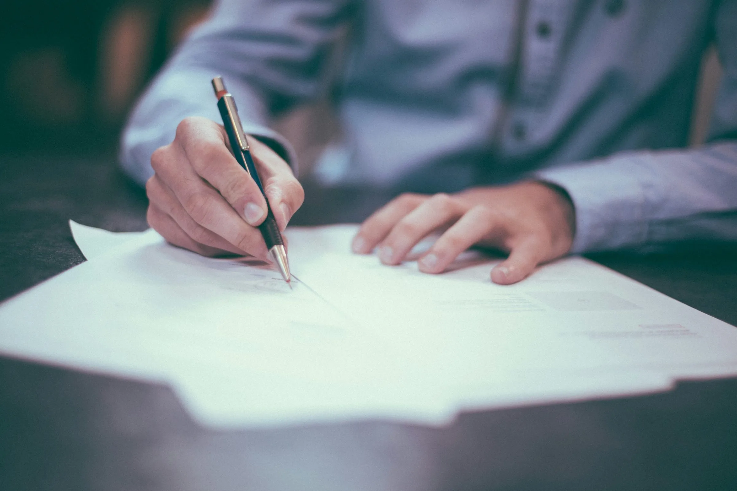 A person at a desk holding a pen over a few printed pages, about to mark them up