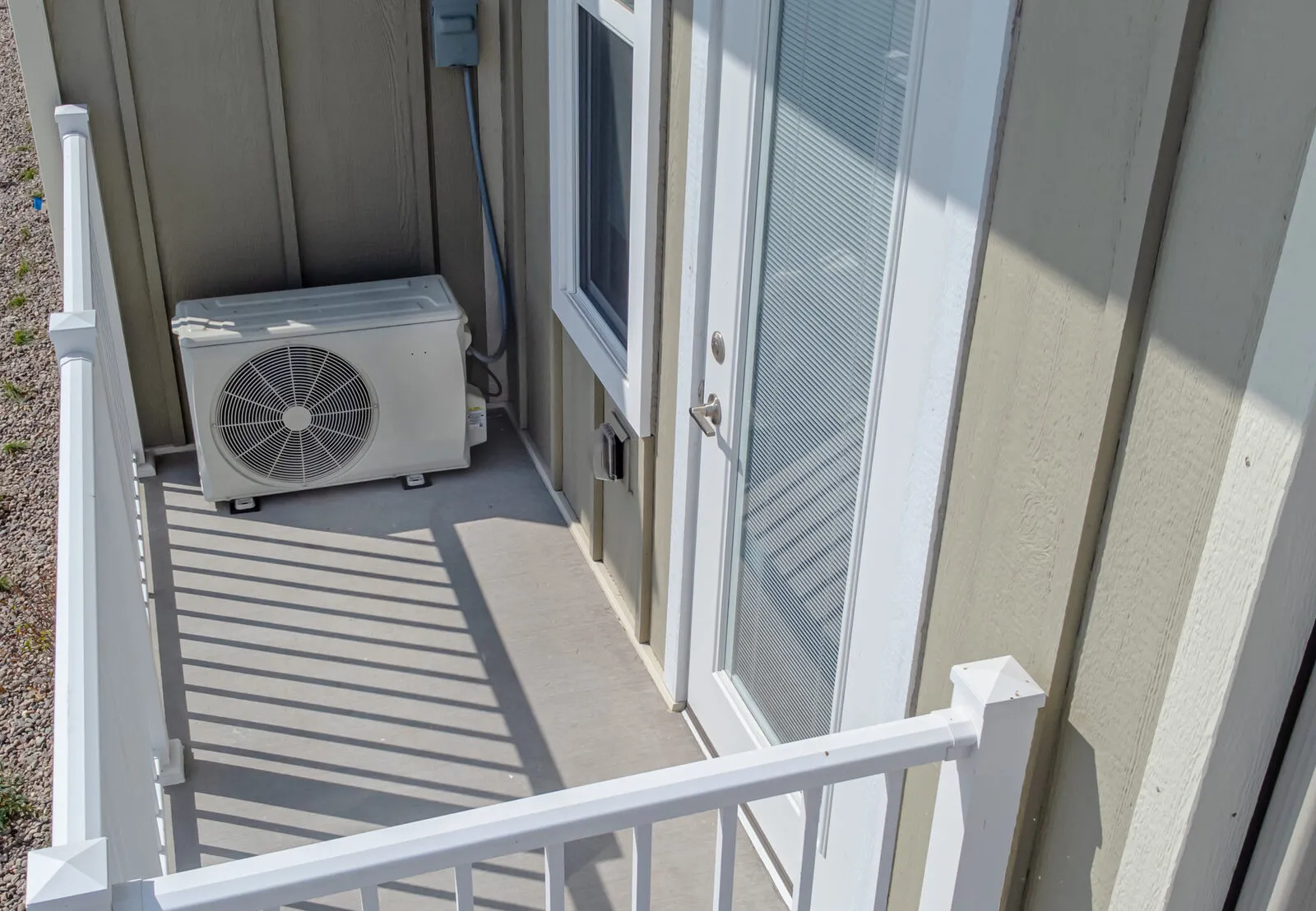 Small outdoor heat pump unit on a balcony landing beside a house door