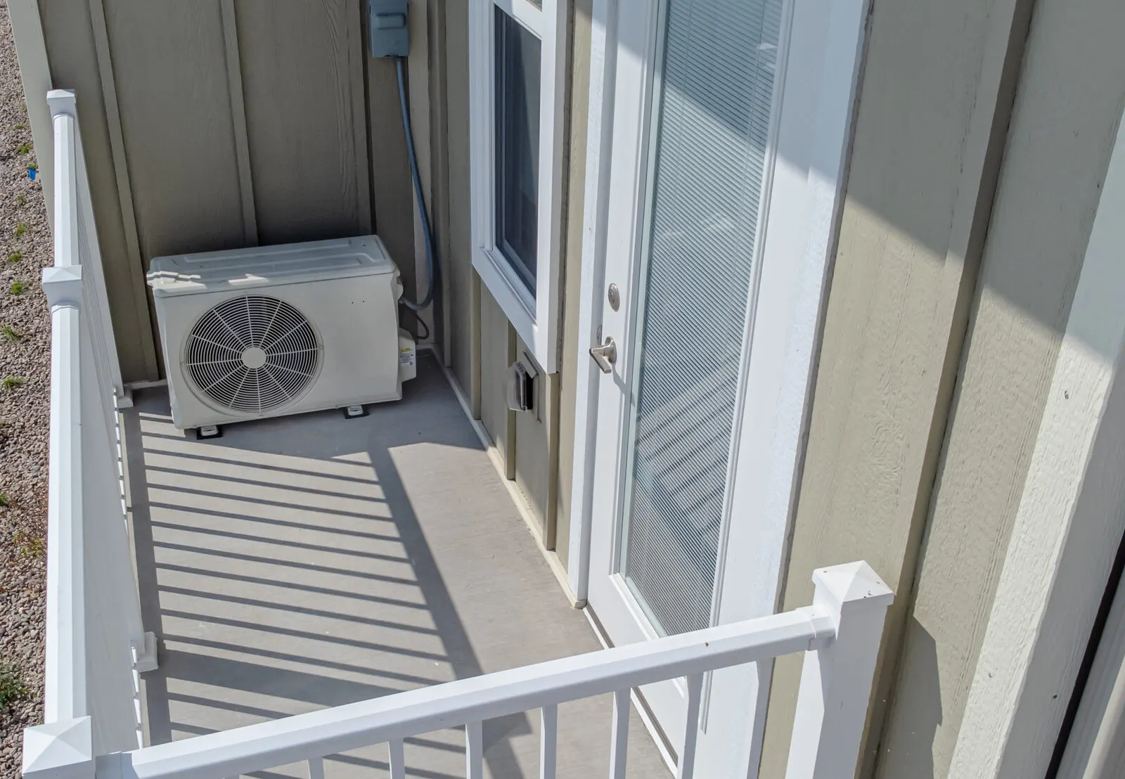 A compact outdoor heat pump unit on a landing beside a house door.