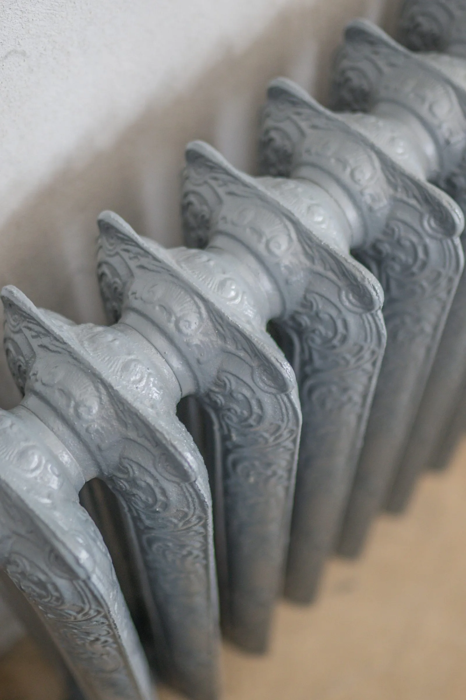 Close view of an ornate cast iron radiator painted silver gray, with raised scrollwork on every section