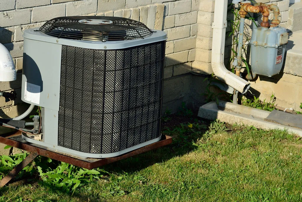 Outdoor air conditioner condenser unit sitting on a pad beside a house wall