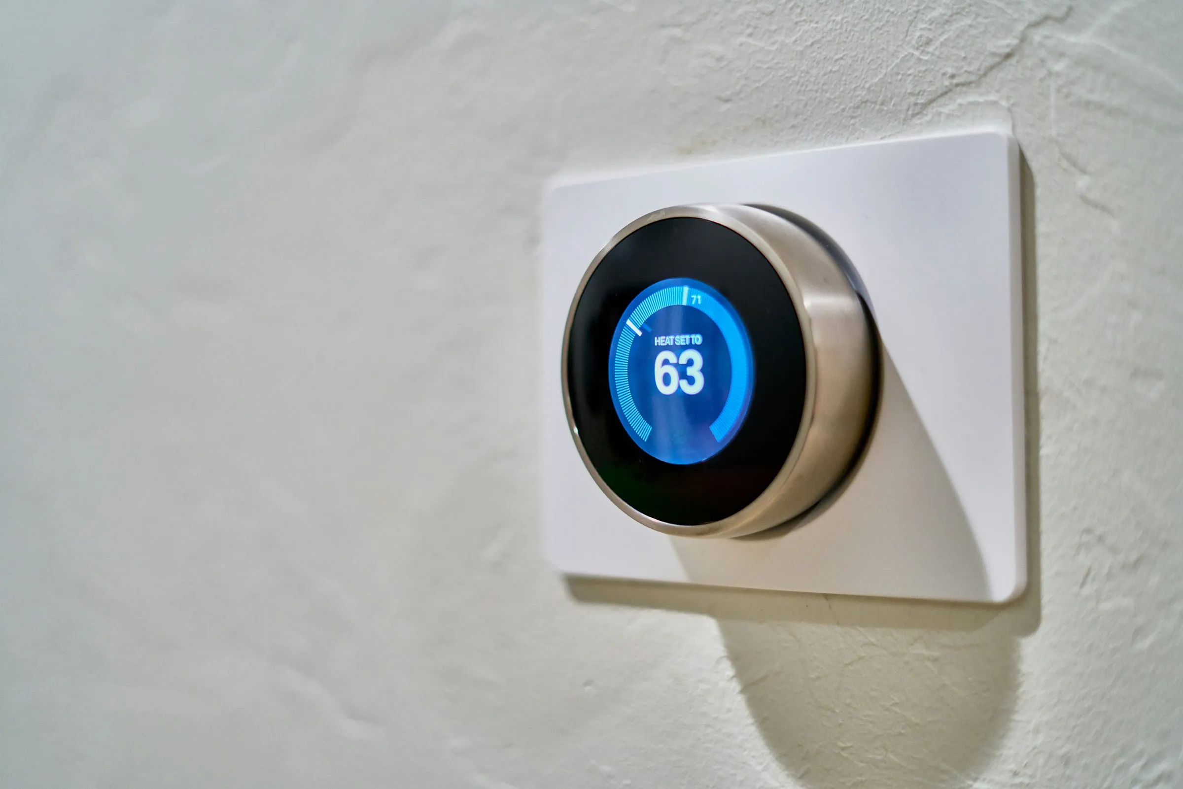 Round digital thermostat on a white wall plate with its screen reading Heat set to 63, and 71 marked on the dial