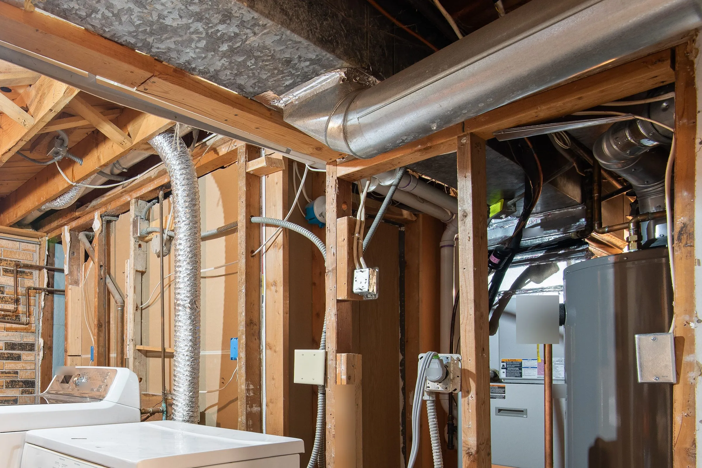 Sheet-metal supply ducts running along a basement ceiling to a gas furnace beside a water heater, the heat source and ducts of a forced air system