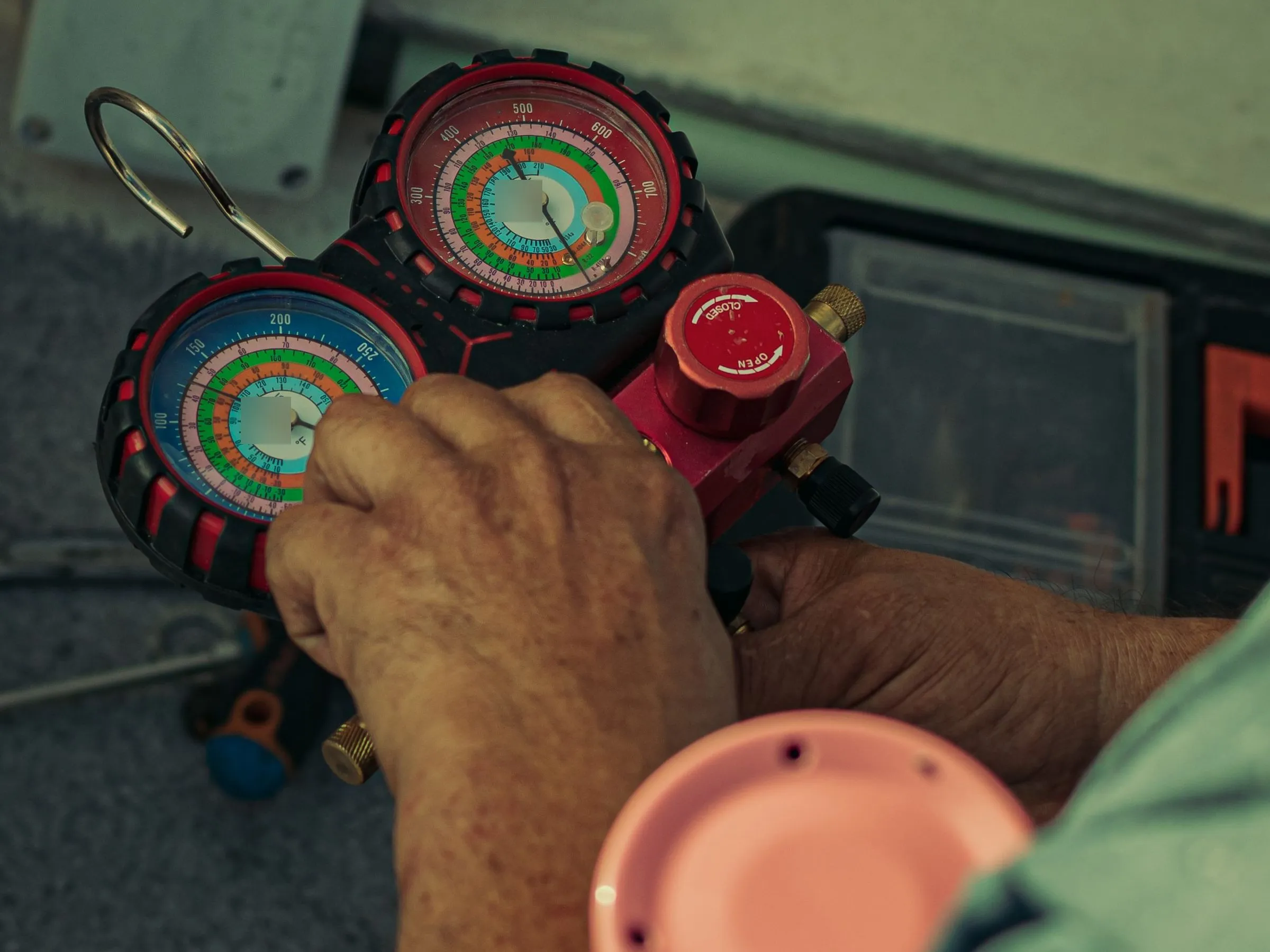 Close-up of a technician's hands holding a refrigerant manifold gauge set with red high-side and blue low-side pressure dials
