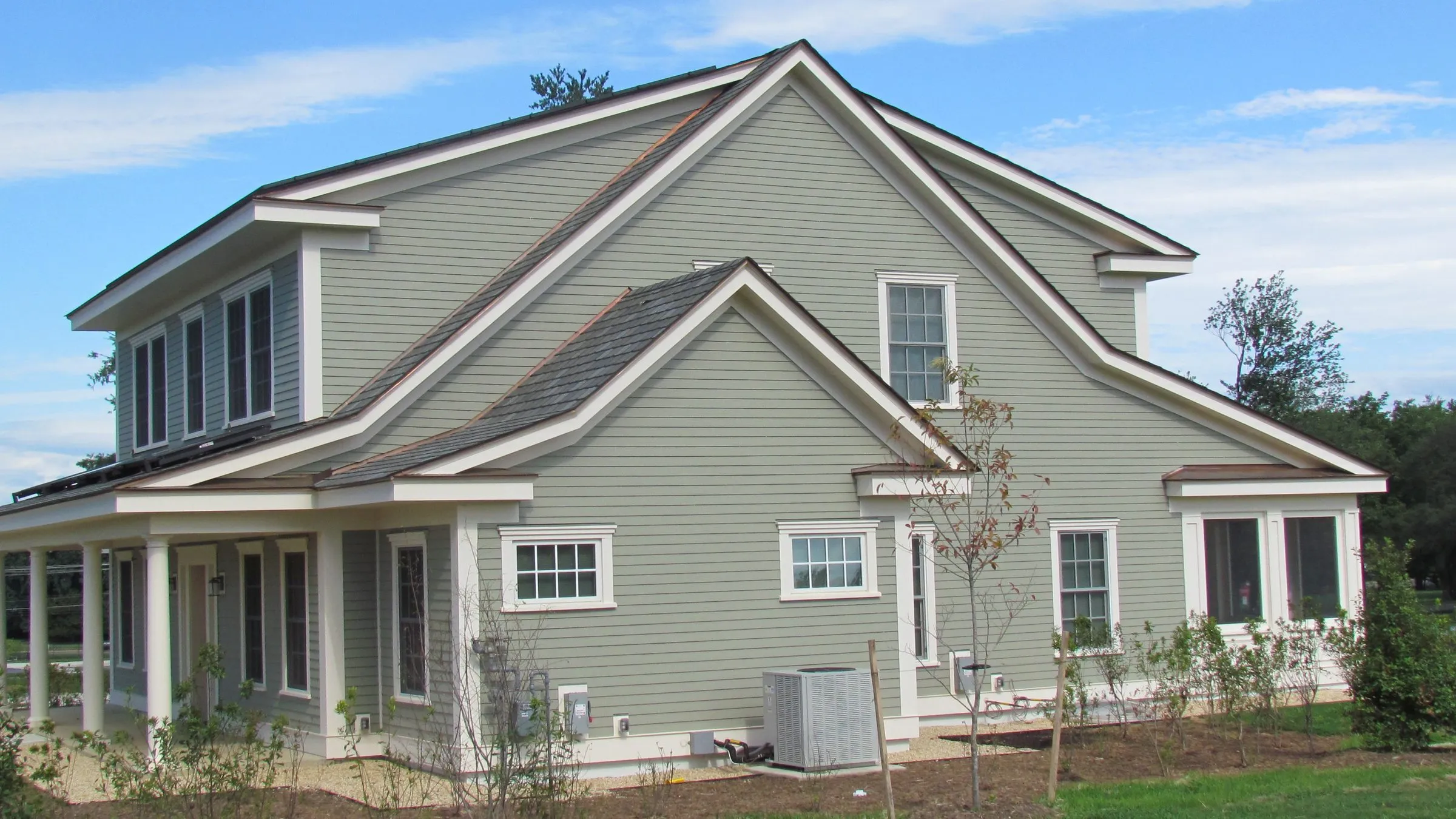Two-story house with green lap siding and an outdoor heating and cooling unit on a pad beside its side wall