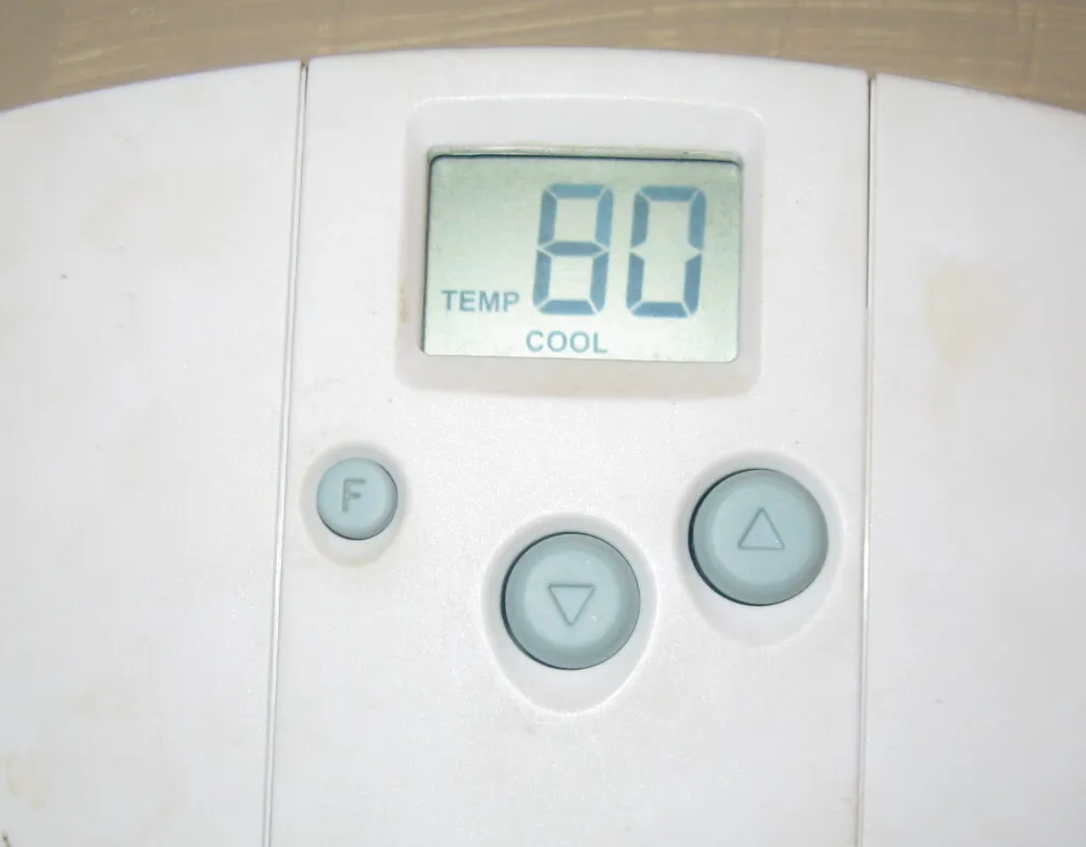 A white wall thermostat with a digital display reading 80 in cooling mode