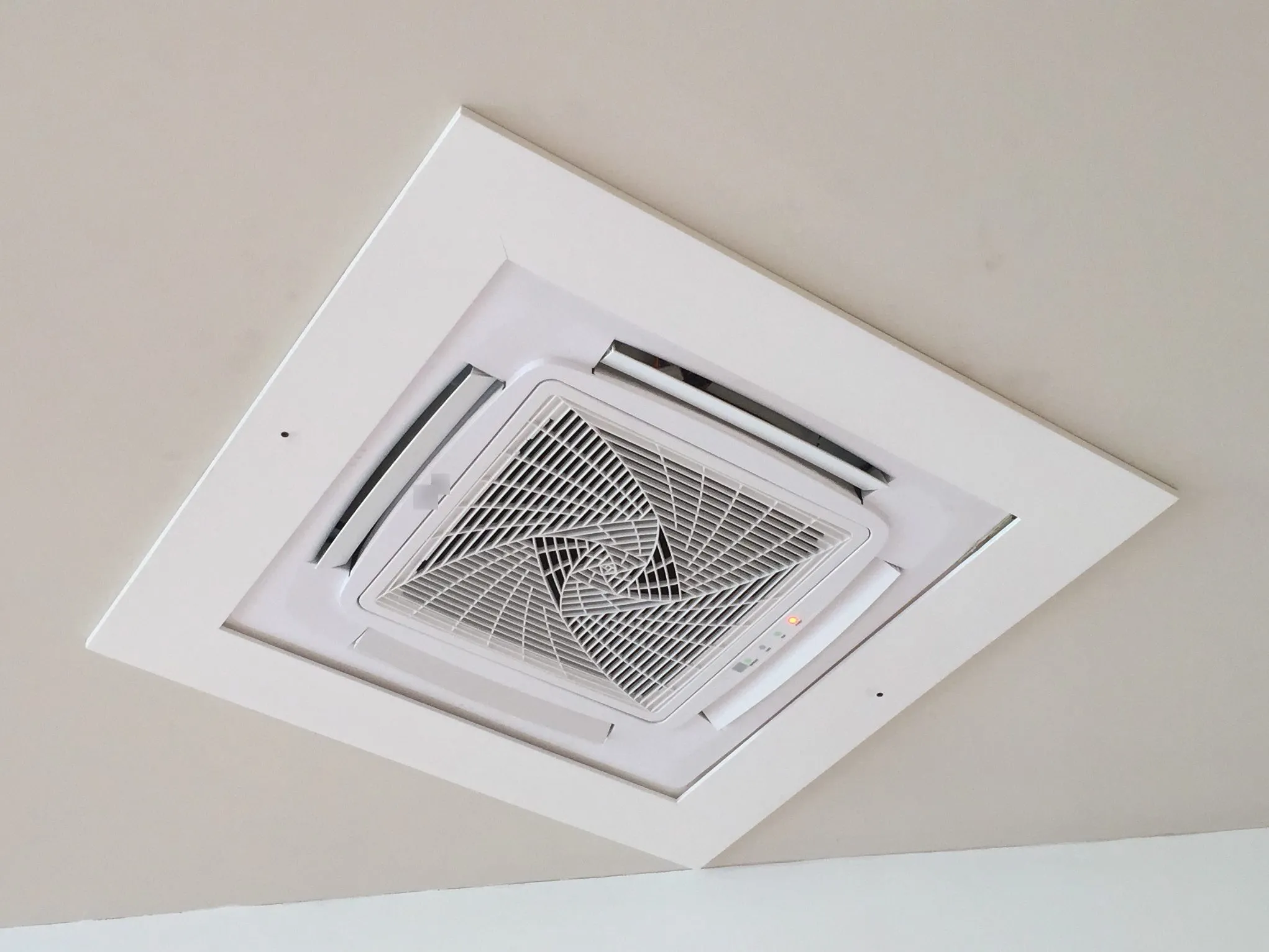 White square ceiling cassette air conditioner set flush into a ceiling, with air vanes on all four sides of a central grille