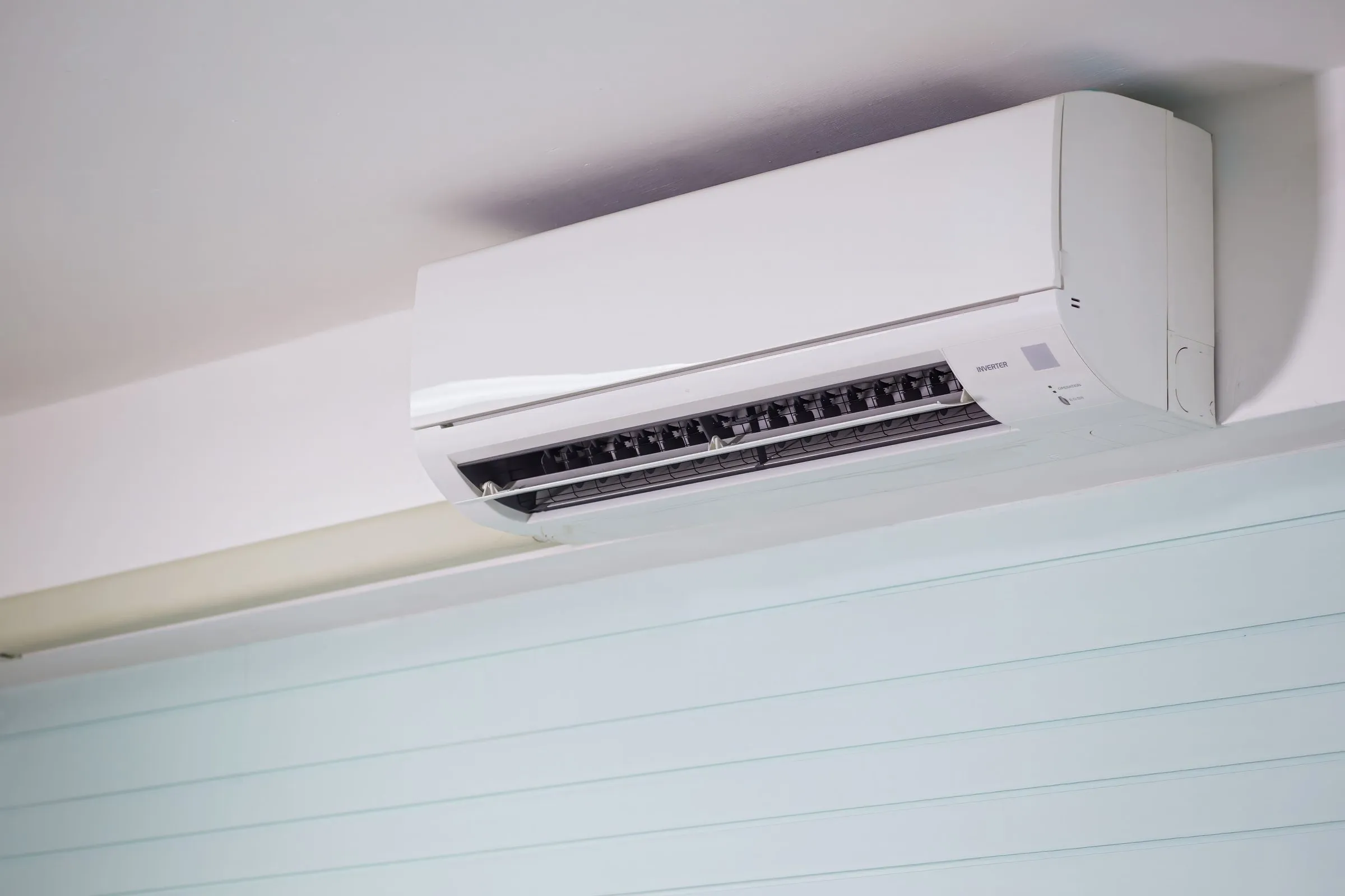 White wall-mounted mini split indoor unit fixed high on a wall just below the ceiling, with its air louver open