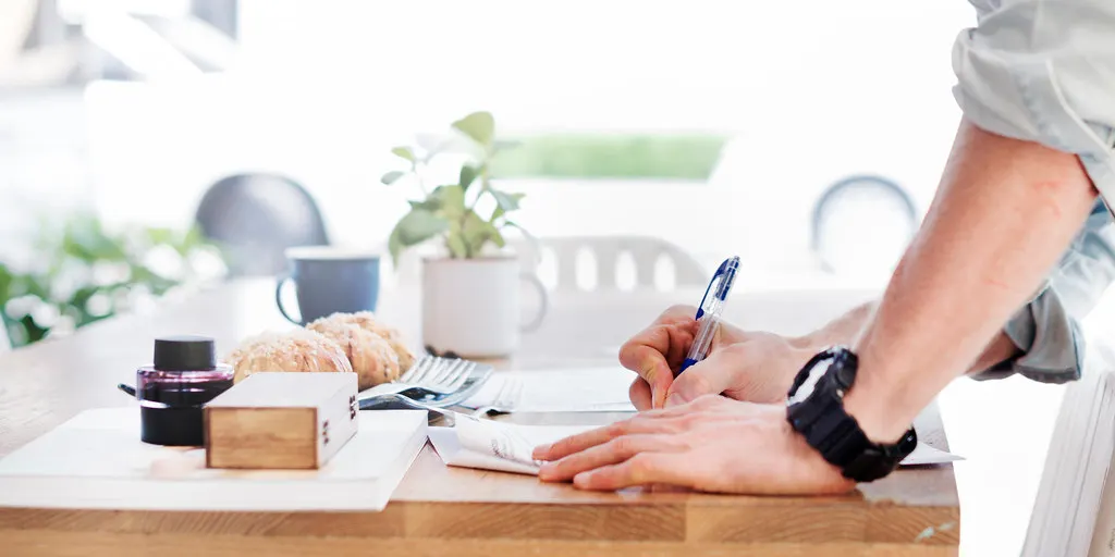 A person writing on paperwork at a kitchen table.